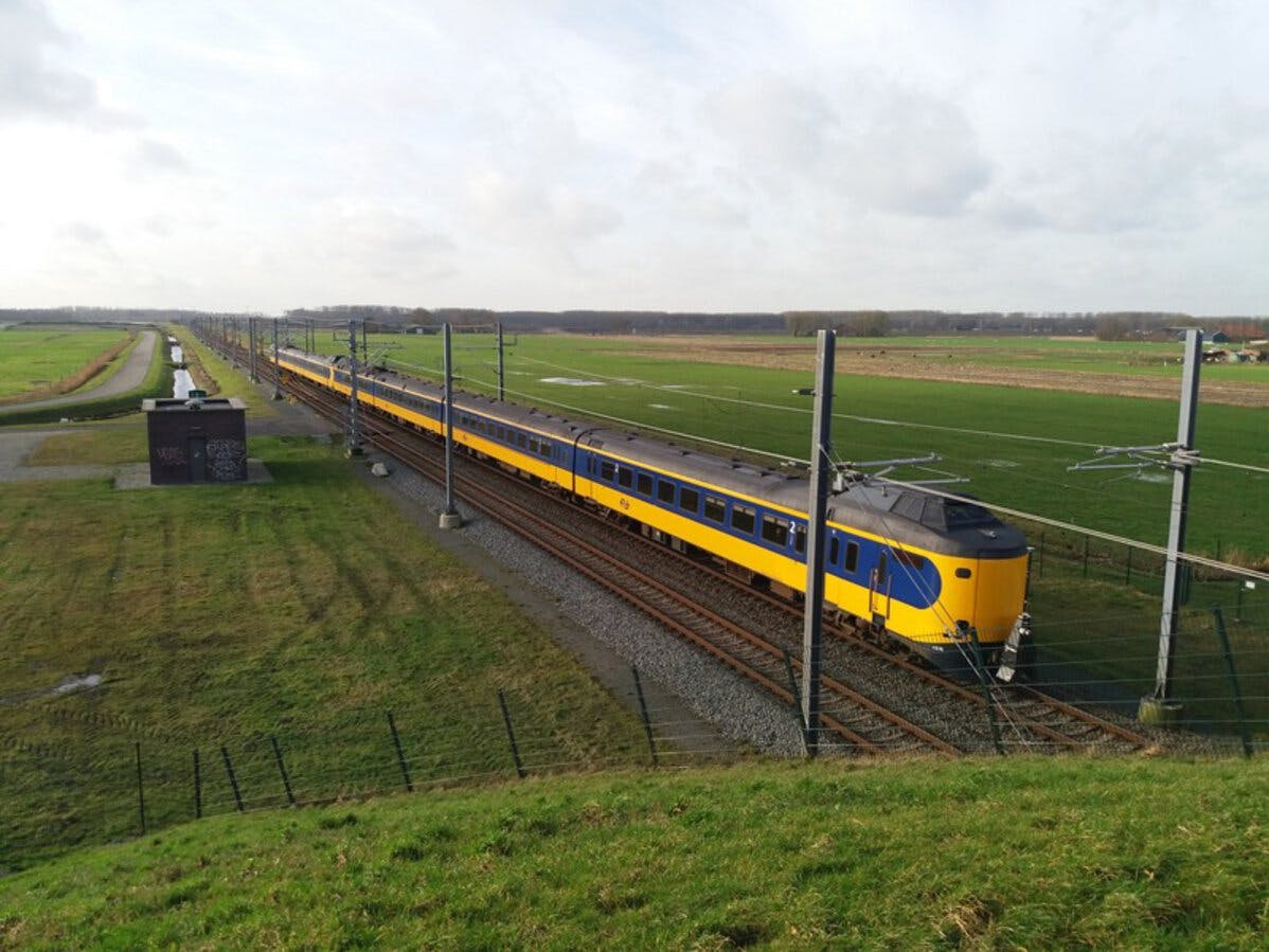 Cross country train for ProRail making its way along the railway tracks with the surrounding areas as flat grassland fields in an isolated location. Railway appears to have been electrified in The Netherlands